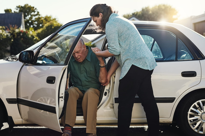 Woman helping senior man out of car
